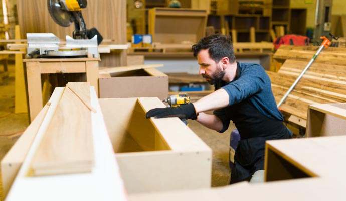 Custom cabinet and furniture making A carpenter in a workshop uses a power drill to assemble custom cabinets from wood and MDF.