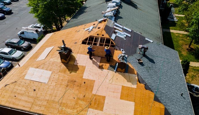 Large-scale roof replacement An aerial view of a large roof replacement project, showing workers tearing off old shingles and installing new plywood sheathing and underlayment.