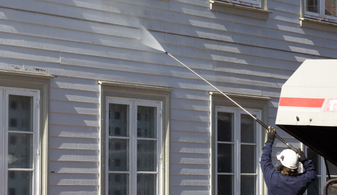 A professional using a pressure washer to clean the exterior of a house